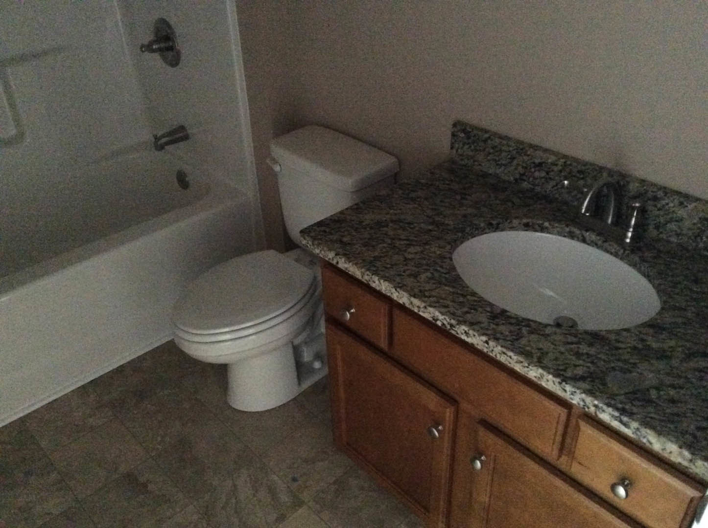 Marble countertop with undermount sink, white toilet, and freestanding bathtub in a modern bathroom with light cabinetry and chrome fixtures
