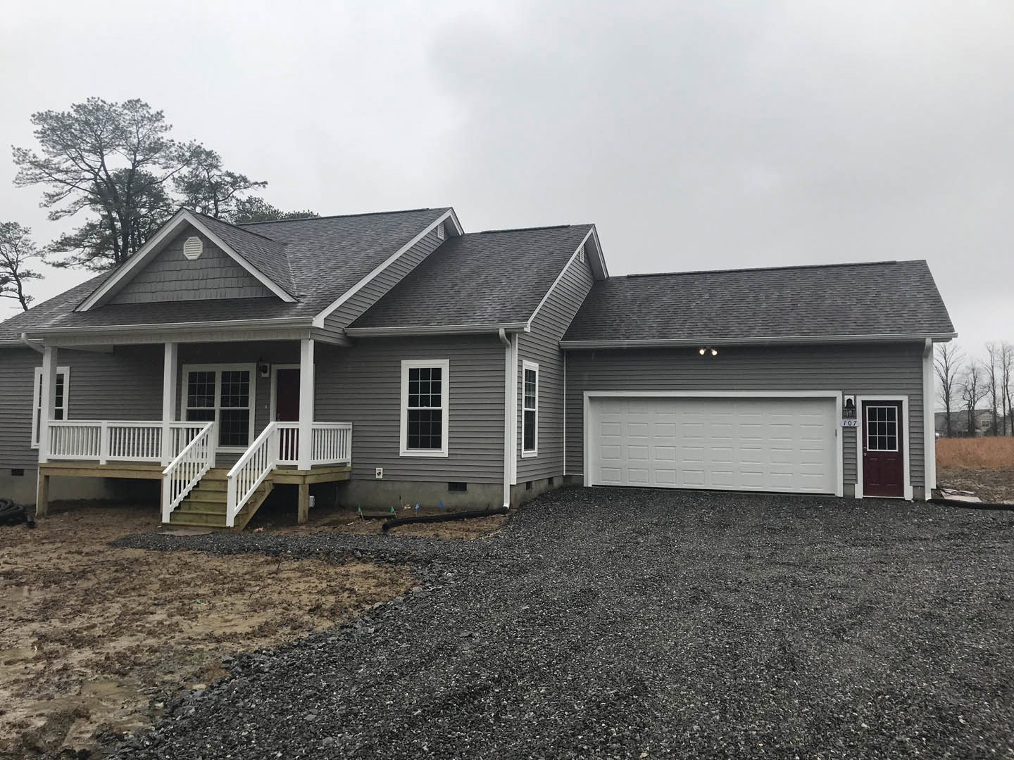 Two-story house with white garage door, grey shingle roof, multi-pane windows, front door with glass insert, and white railing along porch; concrete driveway bordered by lawn and