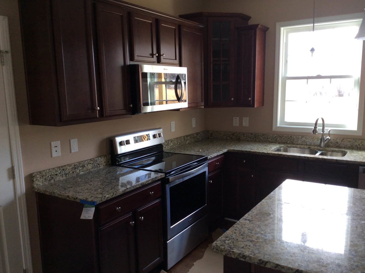 Granite countertops and matching backsplash in a modern kitchen with stainless steel stove, built-in microwave, white cabinetry, and sunlight streaming through a window