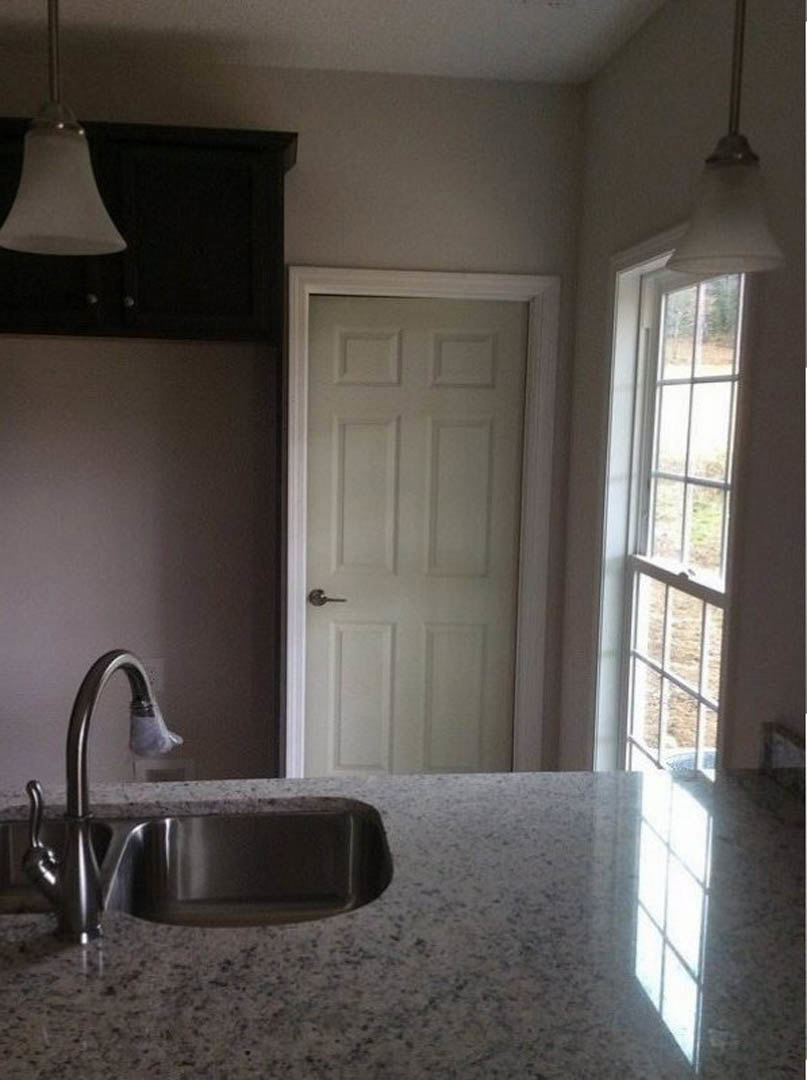 Modern kitchen with tile backsplash, stainless steel faucet and sink set in a stone countertop, white cabinetry, and a white door with silver handle