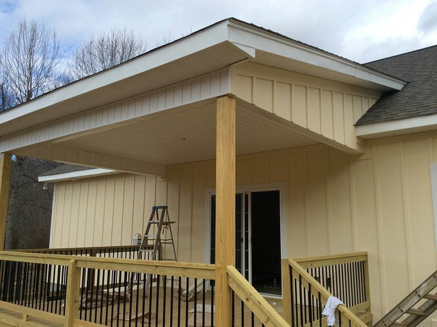 Wooden porch with railing, white towel draped over rail, light-colored siding, gabled roof, outdoor stairs leading to entrance