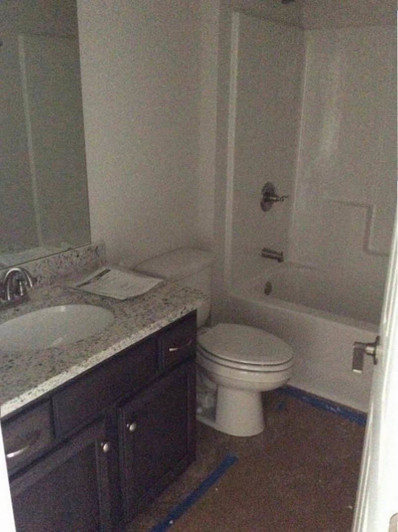 Modern bathroom with white porcelain sink, matching toilet, built-in bathtub, light gray tile walls, chrome faucet, and wood vanity cabinet