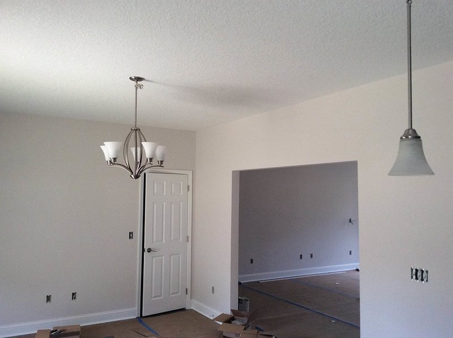 Modern chandelier with multiple glass bulbs suspended from a metal pole, white plaster ceiling and walls, white door with silver handle, light wood flooring