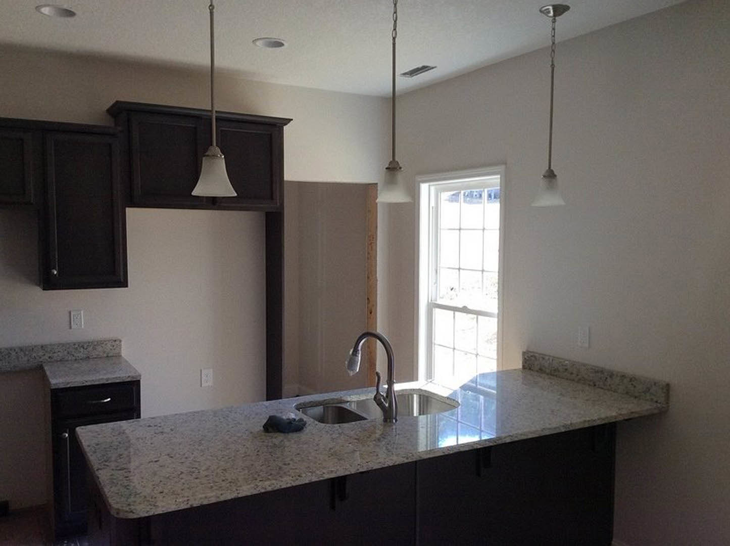 White-framed window above stainless steel sink and faucet set in light kitchen countertop, with neutral cabinetry and modern plumbing fixtures