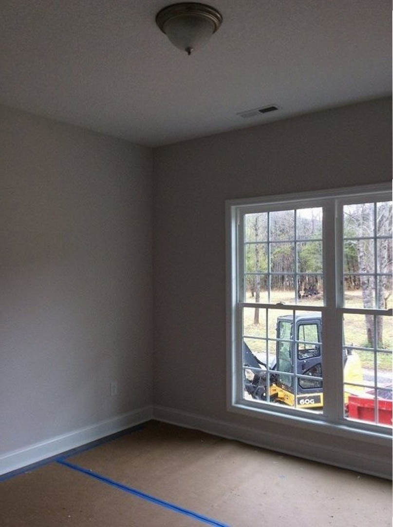 Unfinished room with plaster walls, concrete floor marked by a blue line, ceiling light fixture, large window overlooking construction vehicle and red equipment outside