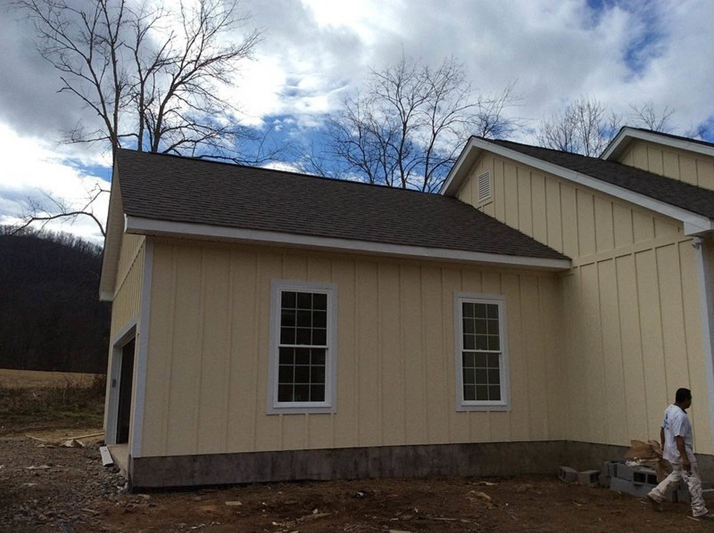 Partially built house with exposed wooden framing, white window frames, and leafless trees under a clear blue sky