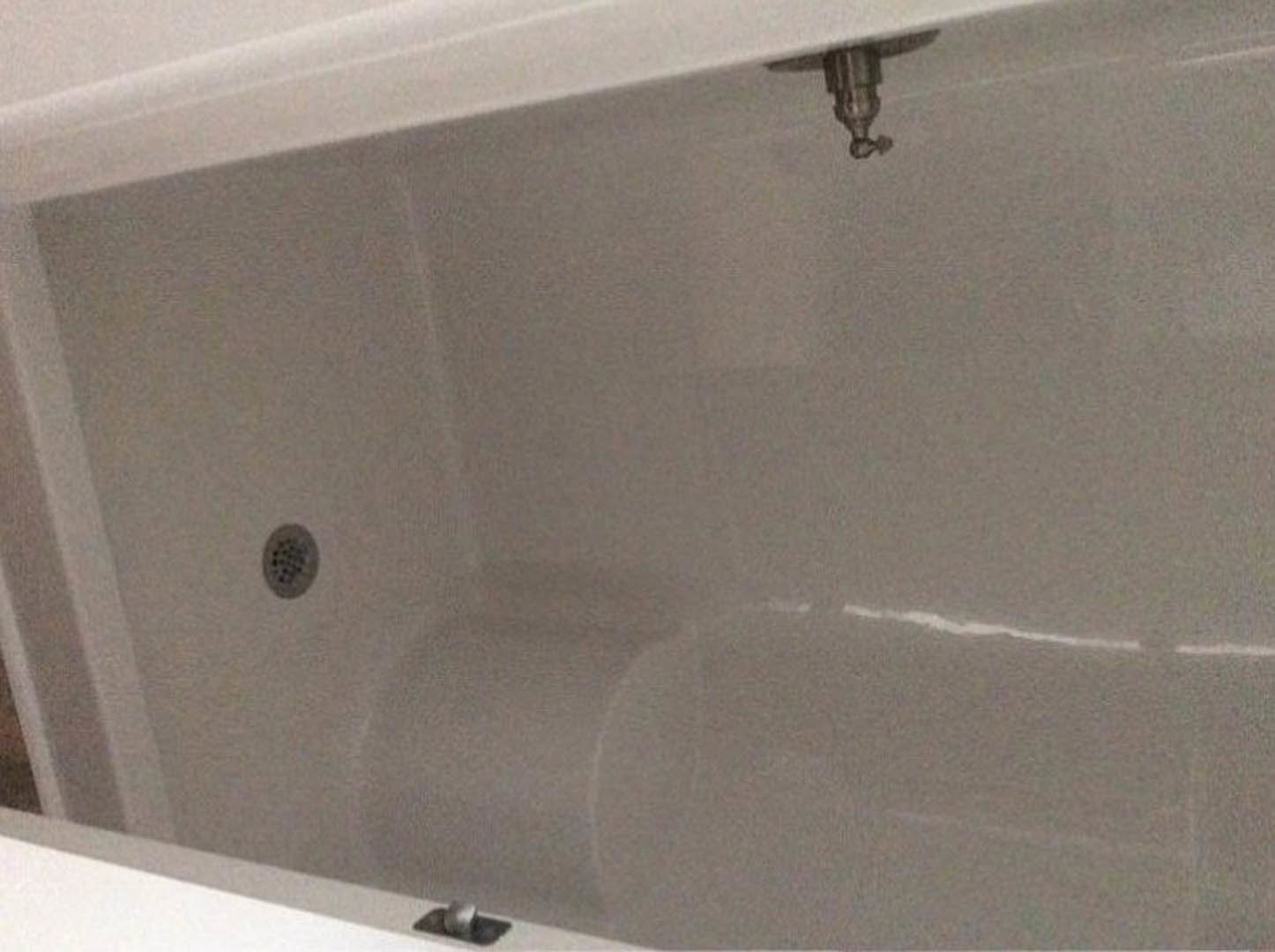 Freestanding white bathtub with chrome drain and spigot against light-colored bathroom wall