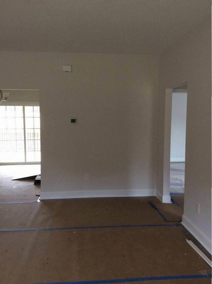 White-walled room featuring a brown laminate floor with a blue accent line, single window with white trim, and a closed white door; wall-mounted light fixture visible.