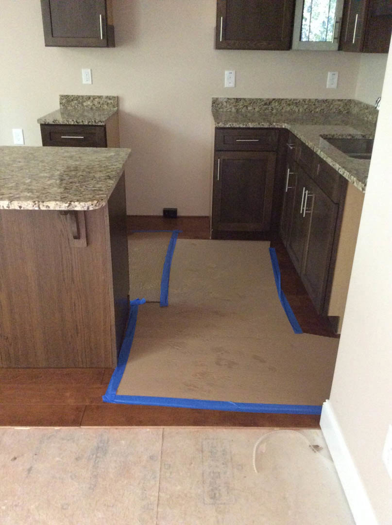 Kitchen with marble countertops marked by blue tape, white cabinetry, tiled flooring, and a window with metal bars.