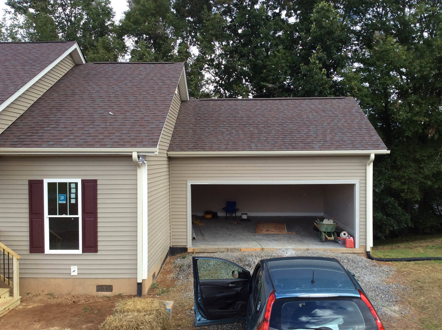 White sedan parked in driveway of a two-story cottage-style home with large windows, wood siding, and mature trees in the yard