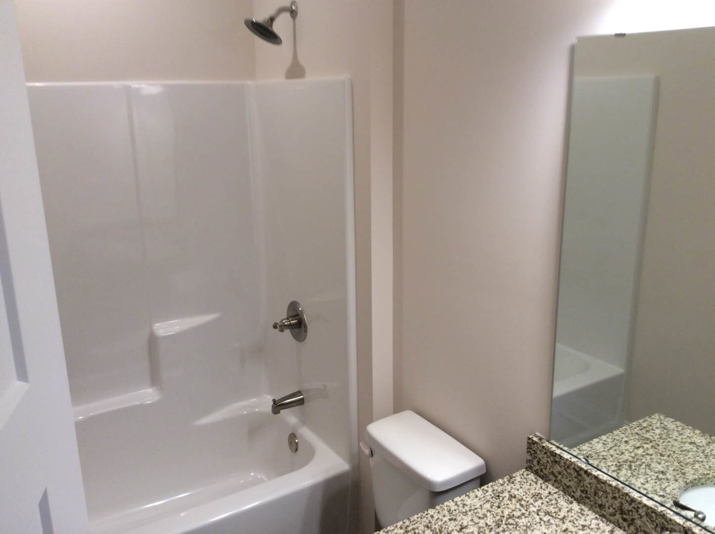 Bathroom with white toilet, marble countertop, silver faucet, tiled walls, and bathtub with chrome fixtures