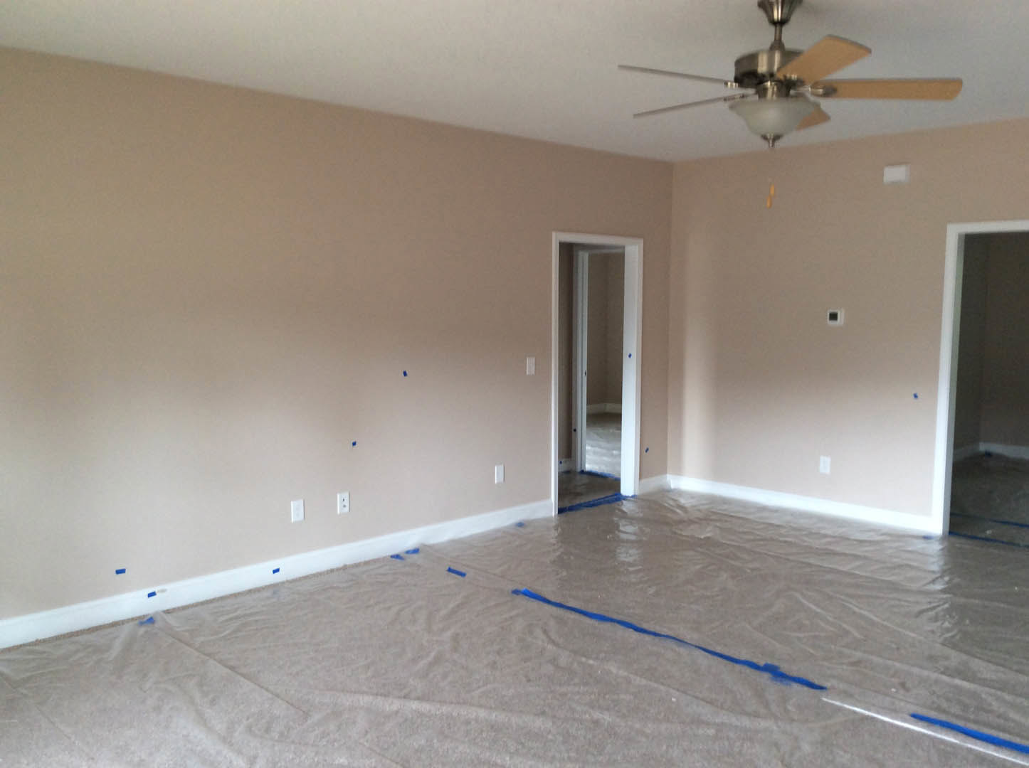 Spacious room with two ceiling fans, light gray walls, glass-paneled door, and floor protected by blue plastic tape