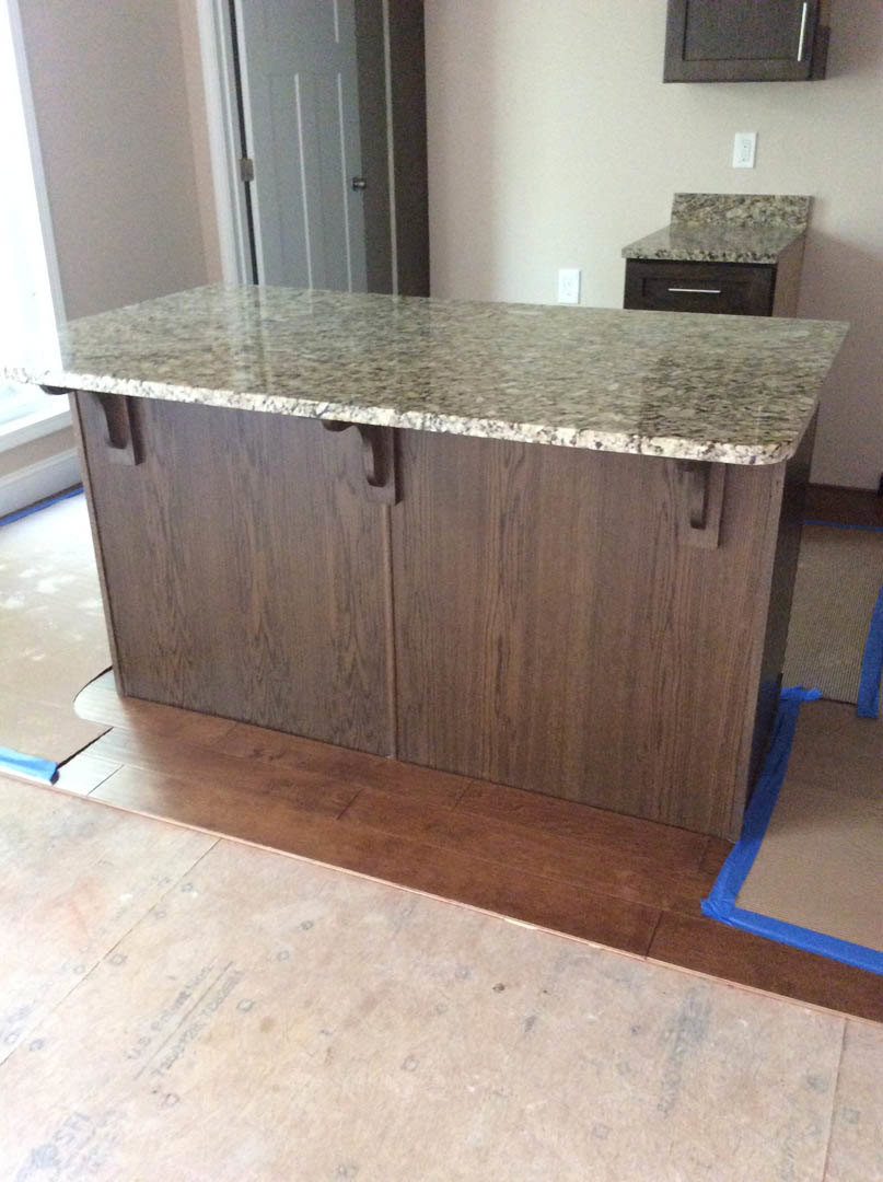 Marble kitchen countertop with grey cabinetry, tile flooring, and blue tape marking on floor