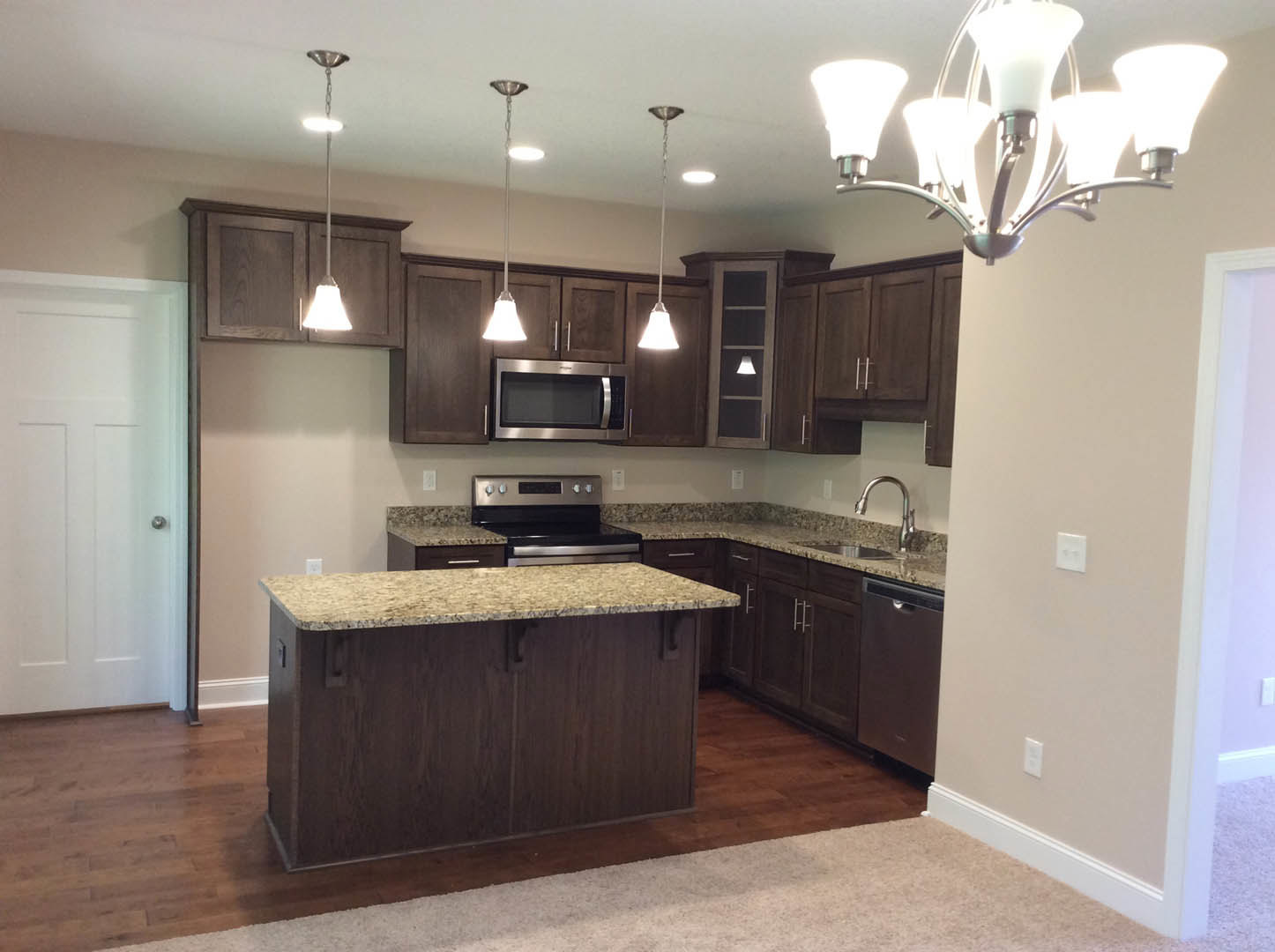 Kitchen with dark wood cabinets, granite island countertop, stainless steel microwave and oven, tile backsplash, pendant chandelier with bell-shaped glass shade, light-colored