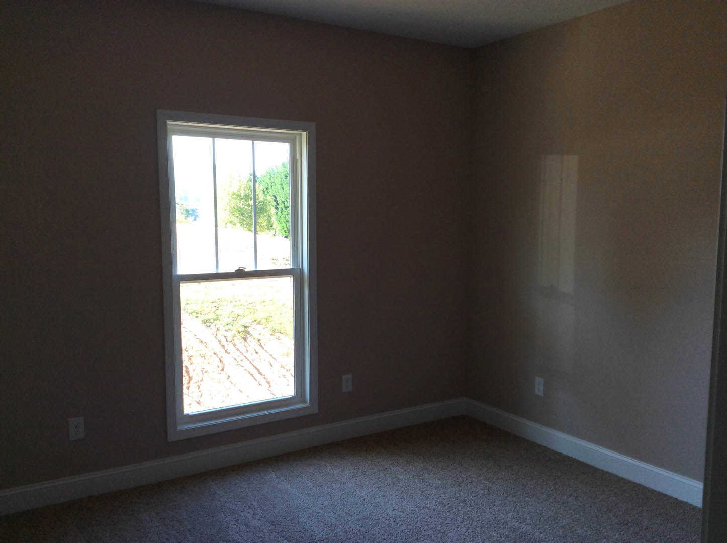 Carpeted room with large window overlooking grassy field, white walls with black accent stripe, natural daylight illuminating interior.