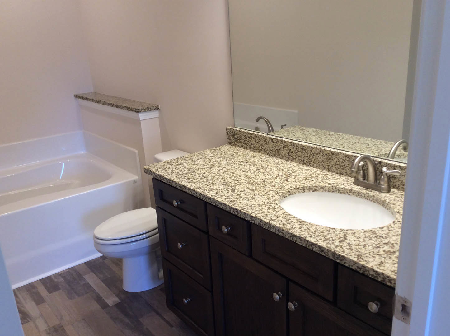 Bathroom with marbled countertop, oval undermount sink, chrome faucet, white toilet, wall-mounted mirror, and light tile flooring