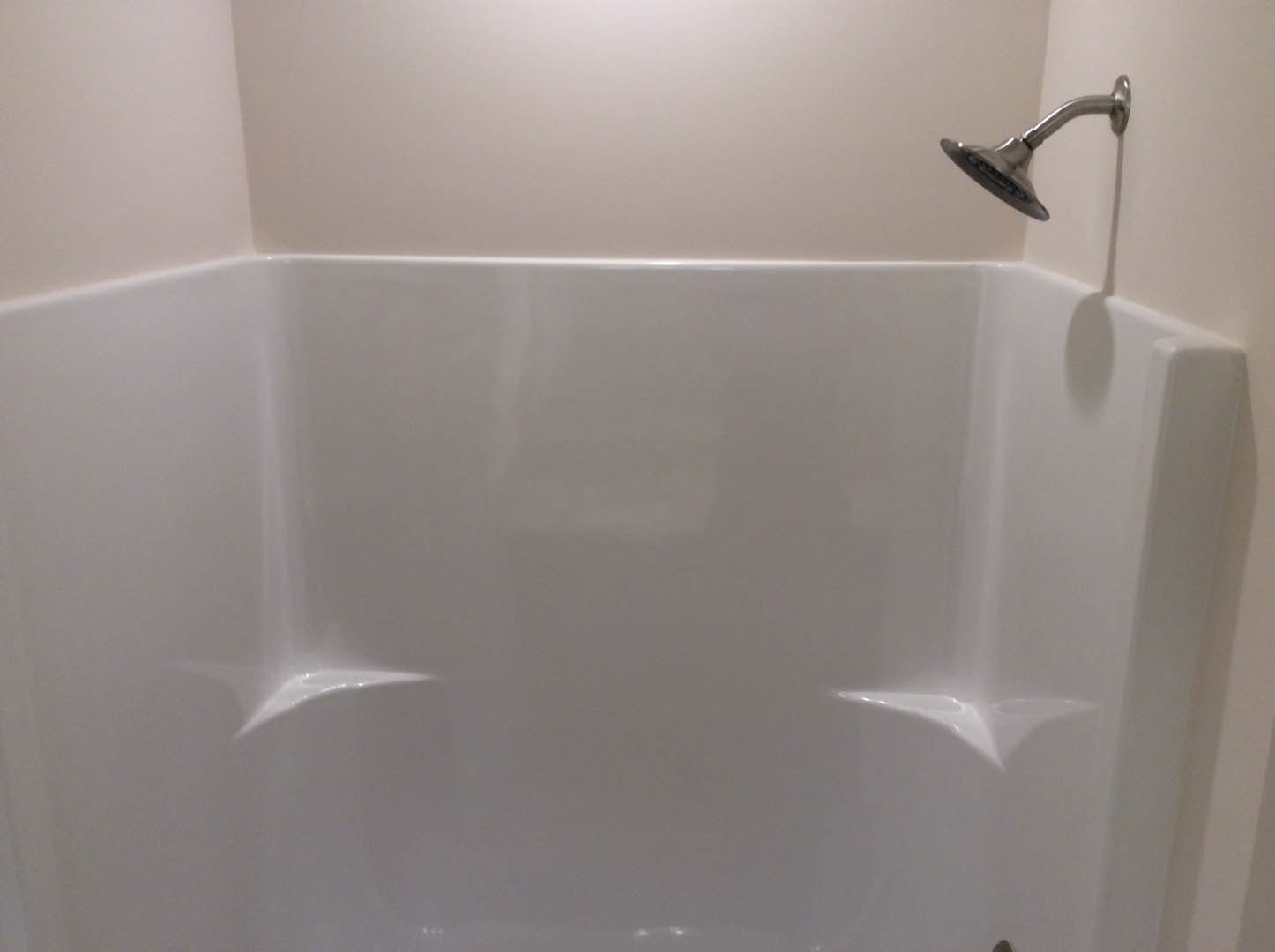 Chrome shower head mounted above a white bathtub, tan tile wall in background
