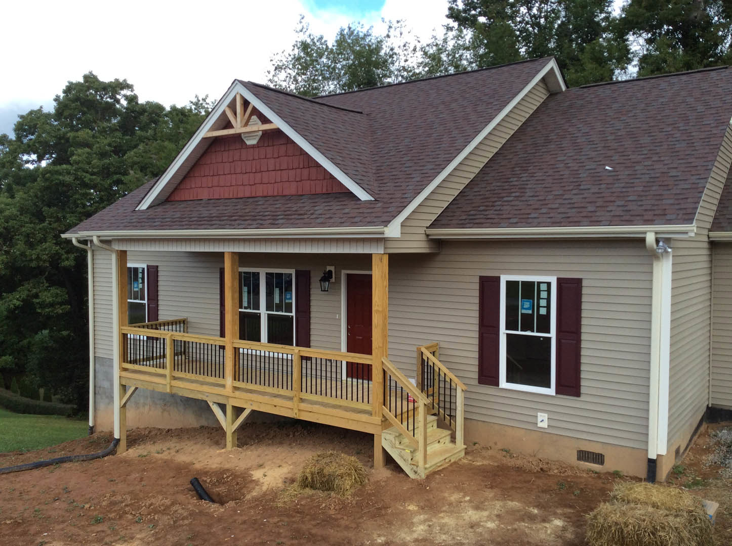 Two-story home with light siding, covered front porch, wooden deck with black railing, white-framed windows, gabled roof, and stairs leading to the yard