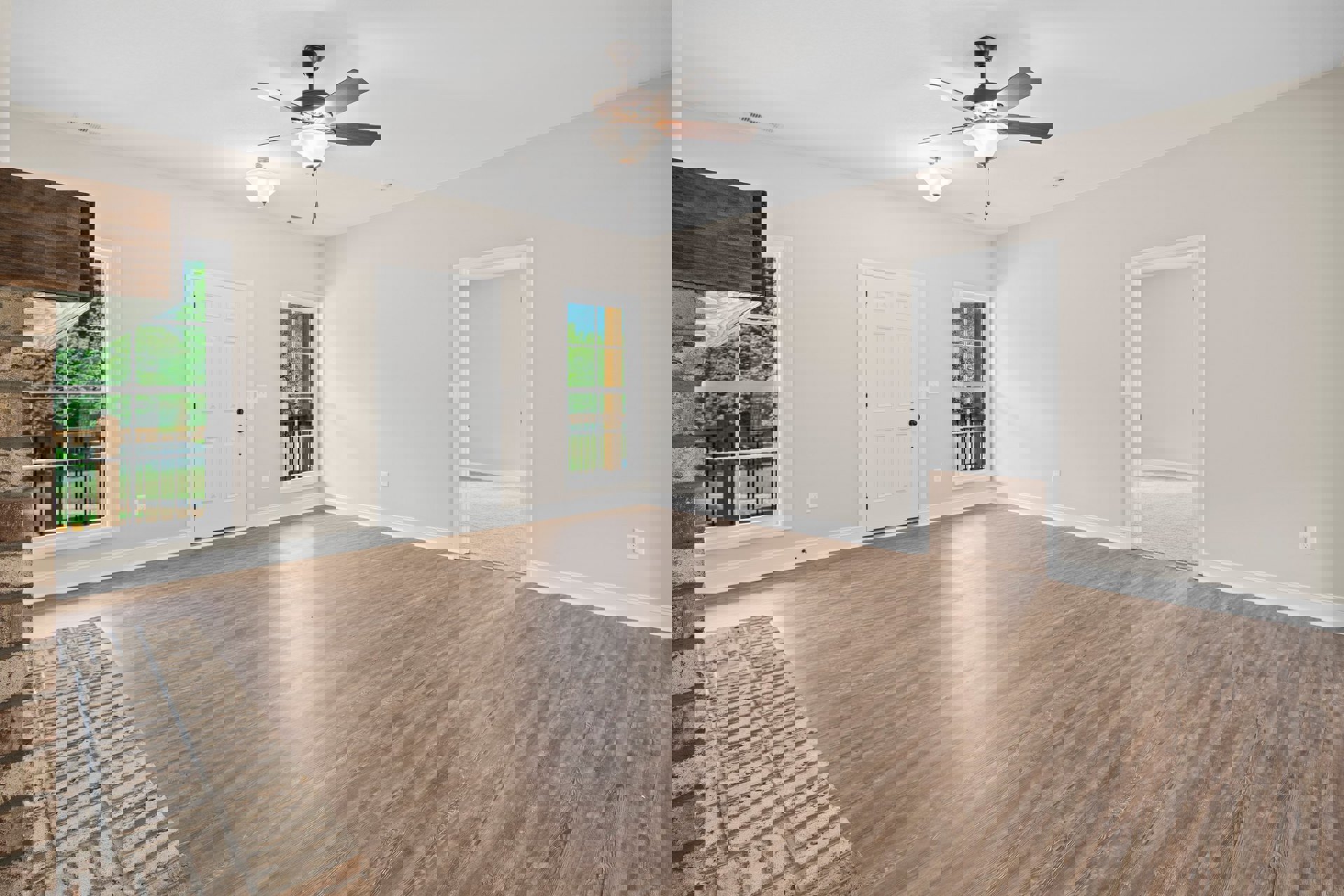 Ceiling fan with light fixture above wood laminate flooring, white walls, white door with black knobs, window overlooking trees.