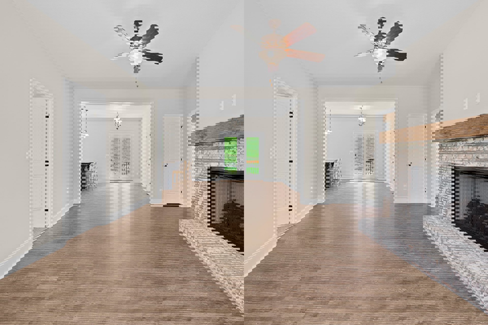 Living room with wood flooring, white walls, ceiling fan with light fixture, fireplace with black screen, white door with black knob, and double glass-paneled doors.