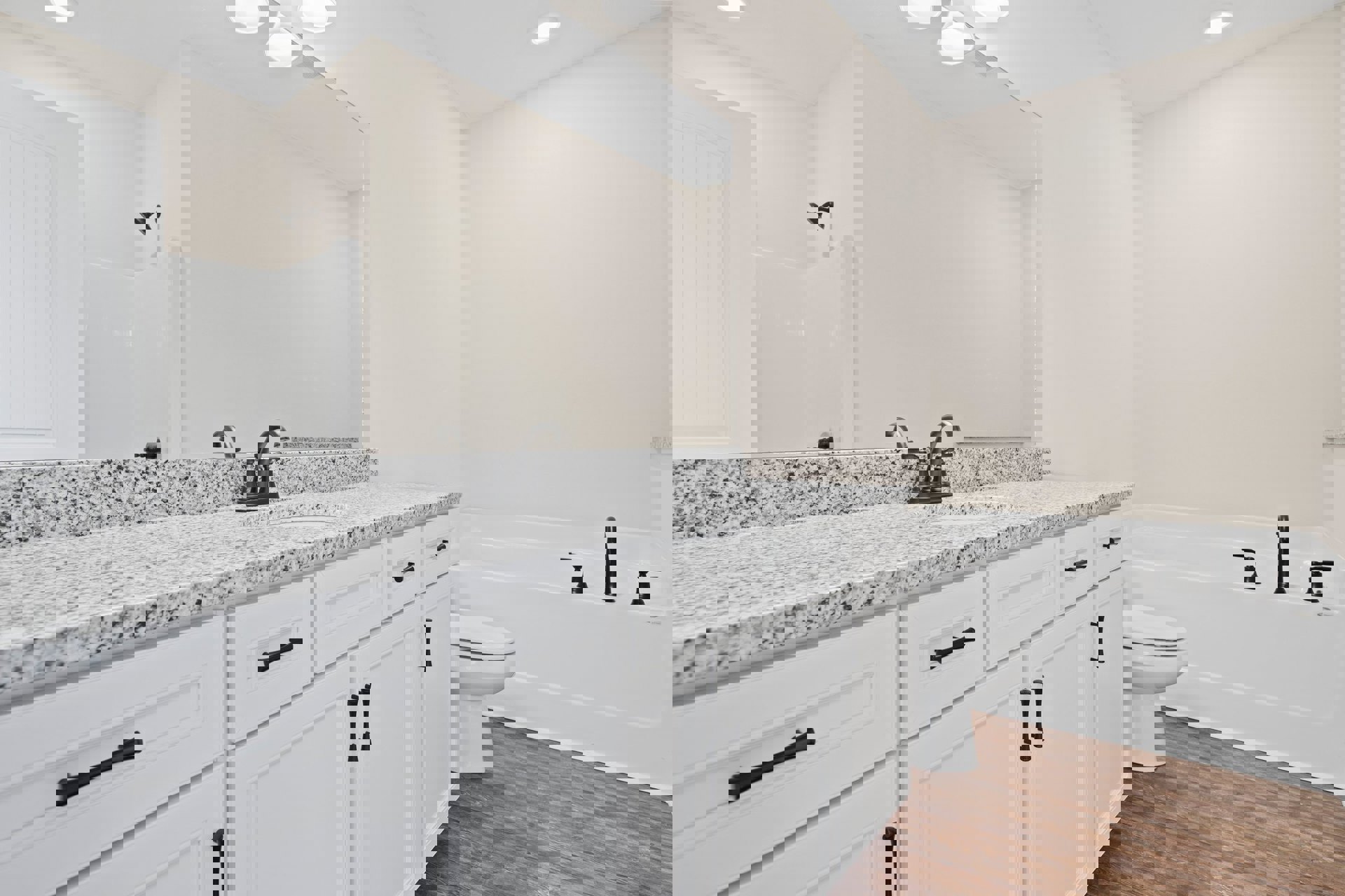 Bathroom with white cabinets, marble countertops, wood flooring, white toilet, black hardware, and white walls