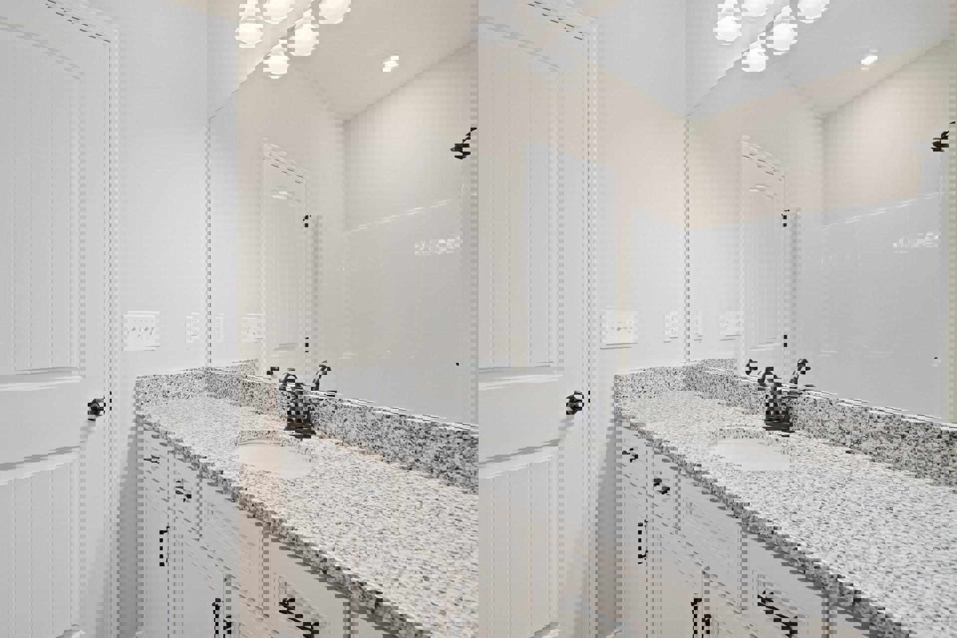 Marble bathroom countertop with undermount sink, chrome faucet, large framed mirror, white cabinetry, and black door handle