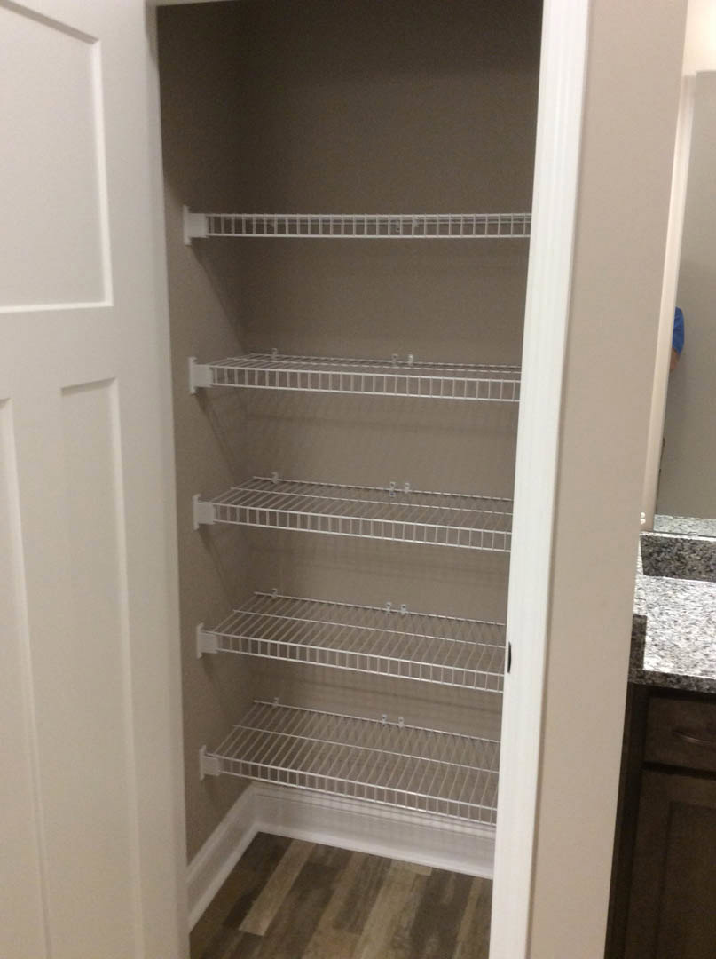 Walk-in closet with white built-in shelves, wood flooring, and white baseboards