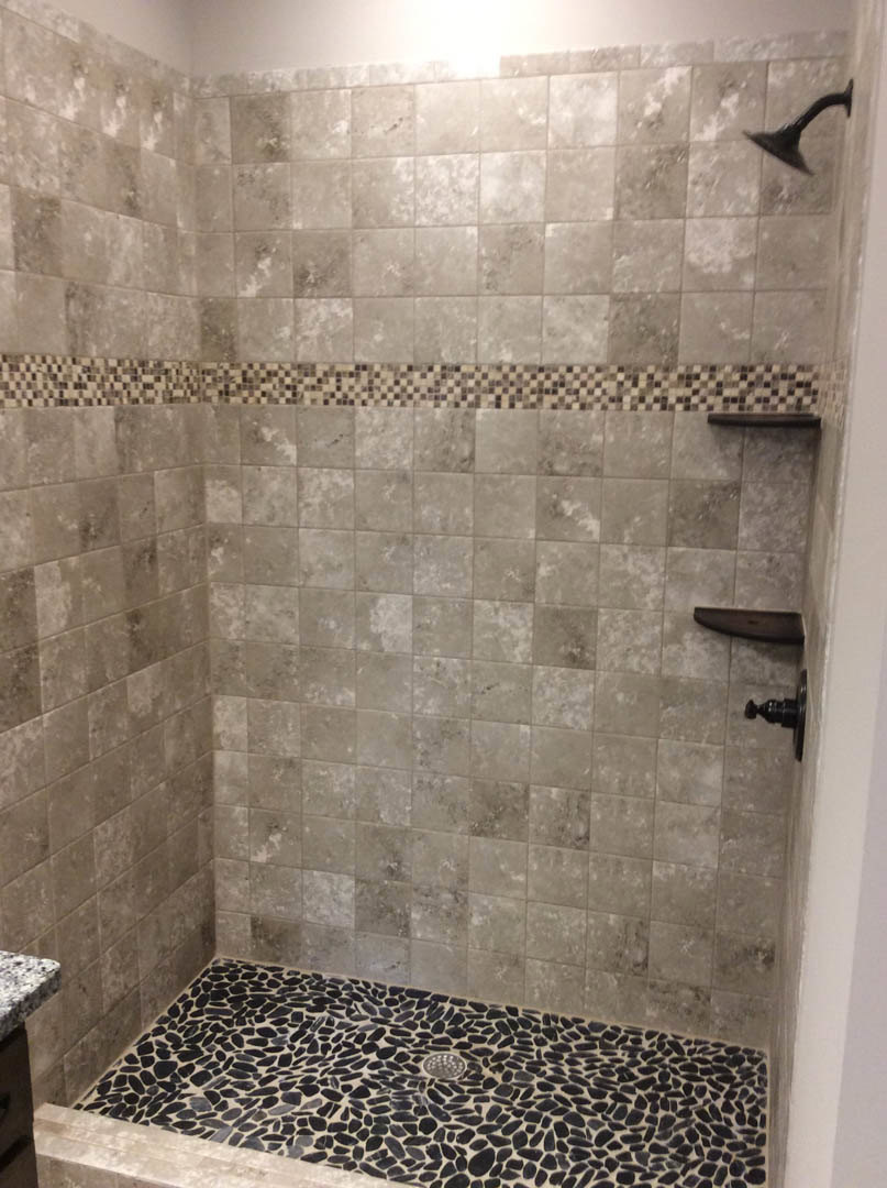 Walk-in shower with chrome shower head, marble tile walls, and matching tile floor with central drain