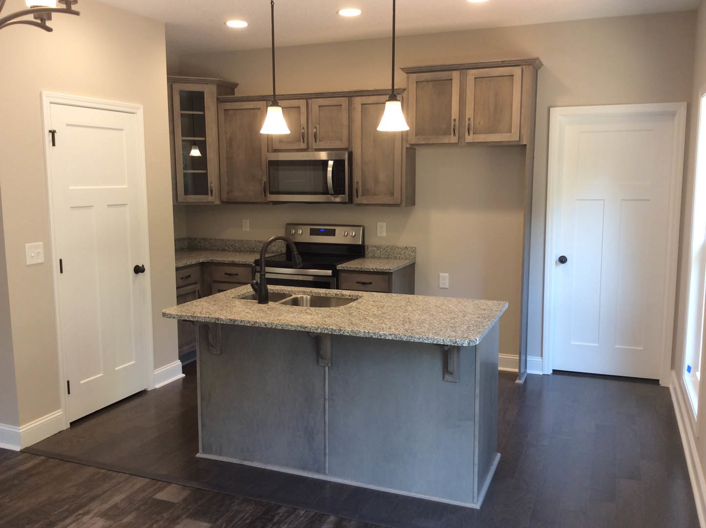Open kitchen with white cabinetry, central island featuring built-in stove and sink, stainless steel microwave, light countertops, and white door with black handle