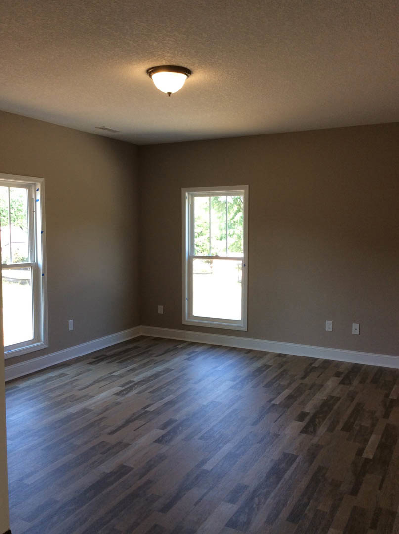 Spacious room with light wood flooring, large windows with white frames, and a modern ceiling light fixture
