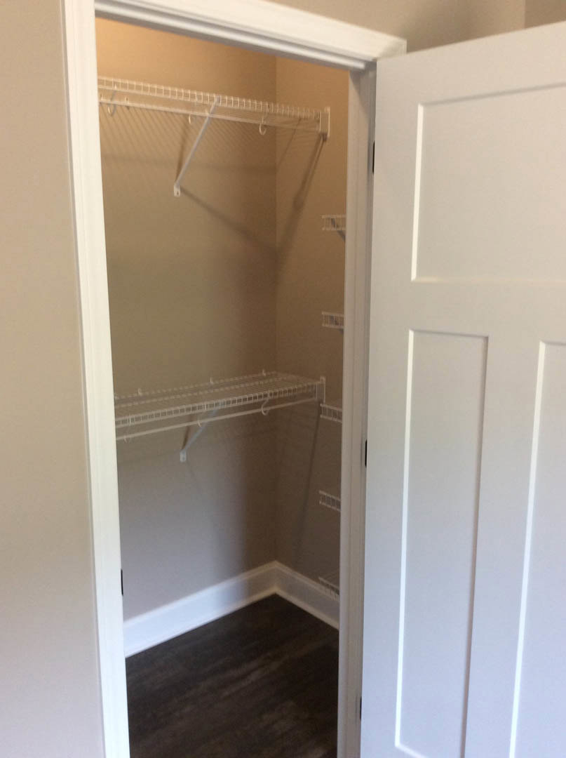 Walk-in closet with white built-in shelves, dark wood flooring, white trim, and a white paneled door
