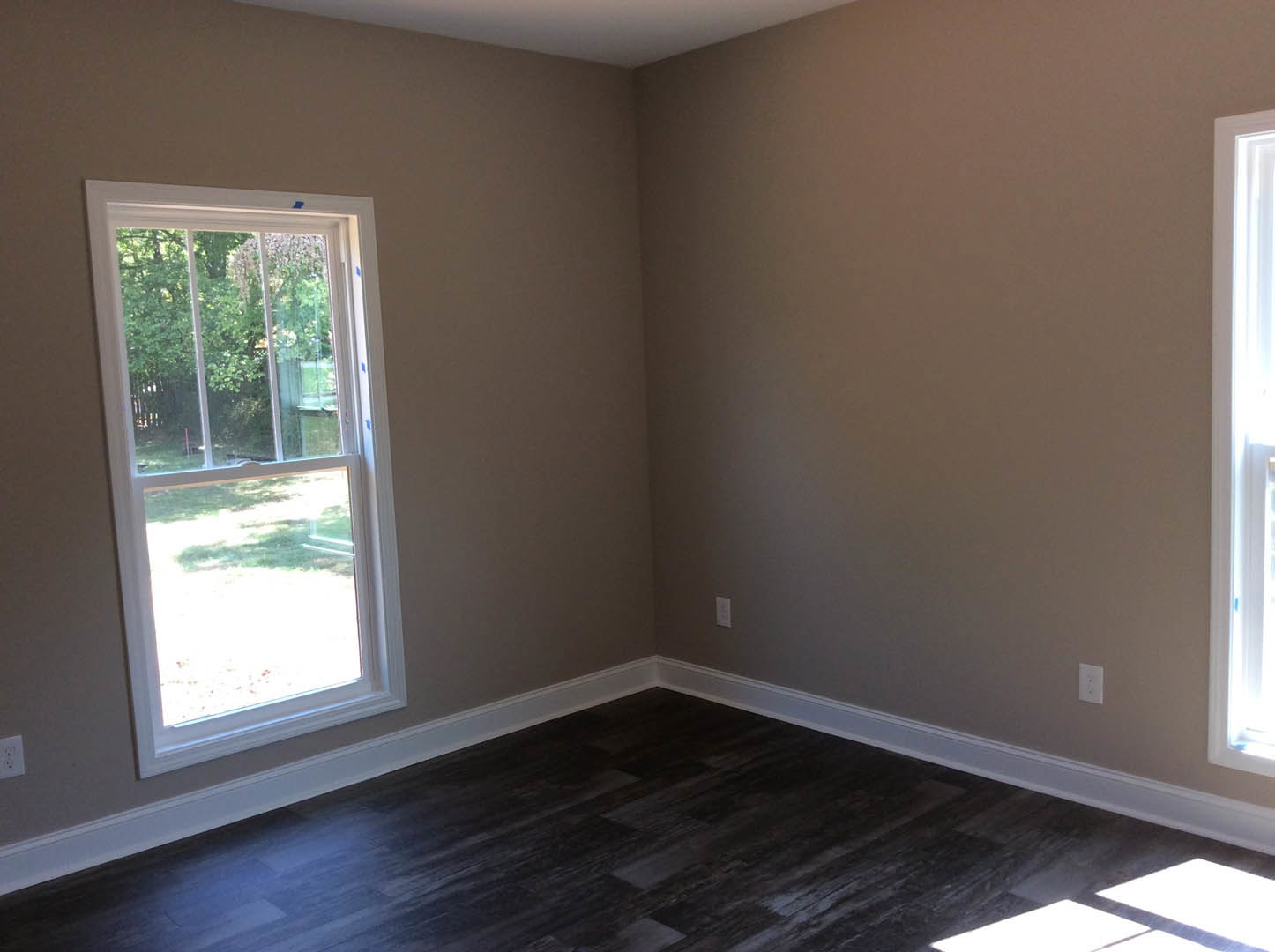 Bright room with large window overlooking grass and trees, dark wood laminate flooring, white baseboards, and white door illuminated by natural light