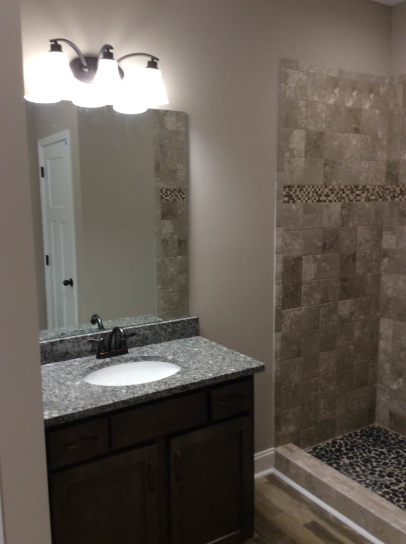 Modern bathroom featuring a white ceramic sink with chrome faucet, glass-enclosed shower with tiled walls, and light fixture above the vanity.