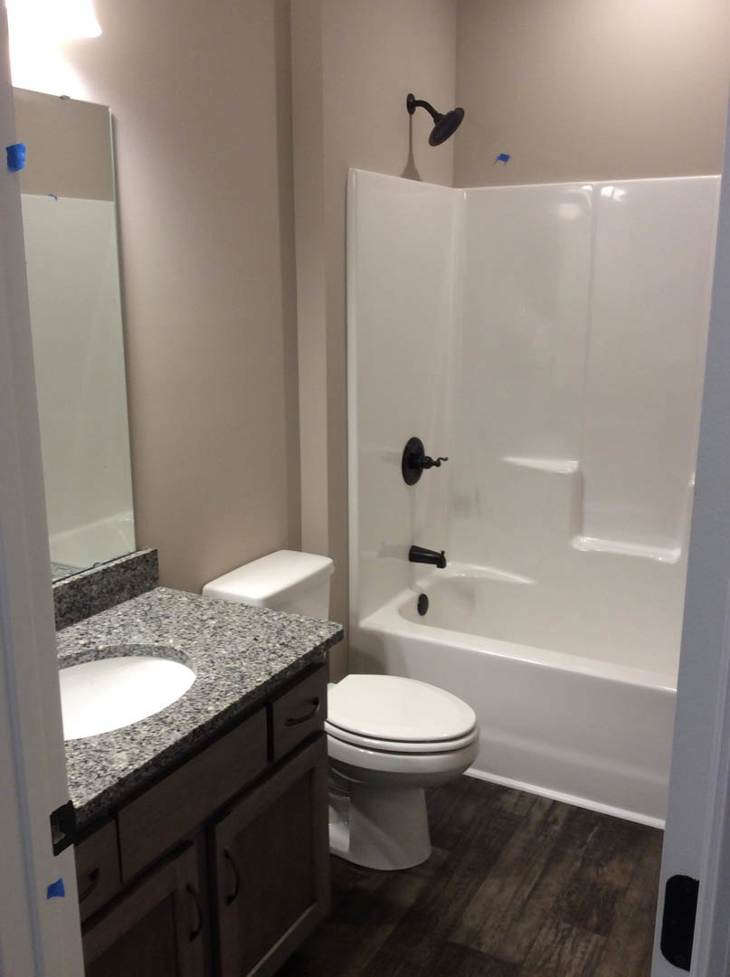 Bathroom with white oval sink, white toilet, freestanding white bathtub with black faucets, wall-mounted shower head, light tile flooring, and white walls
