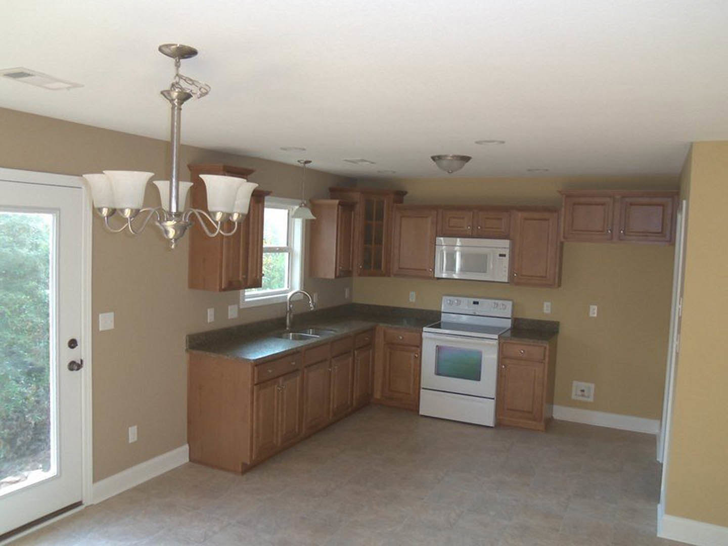 Kitchen with natural wood cabinets, white oven and microwave, stone countertops, stainless steel sink, decorative chandelier, and hardwood flooring