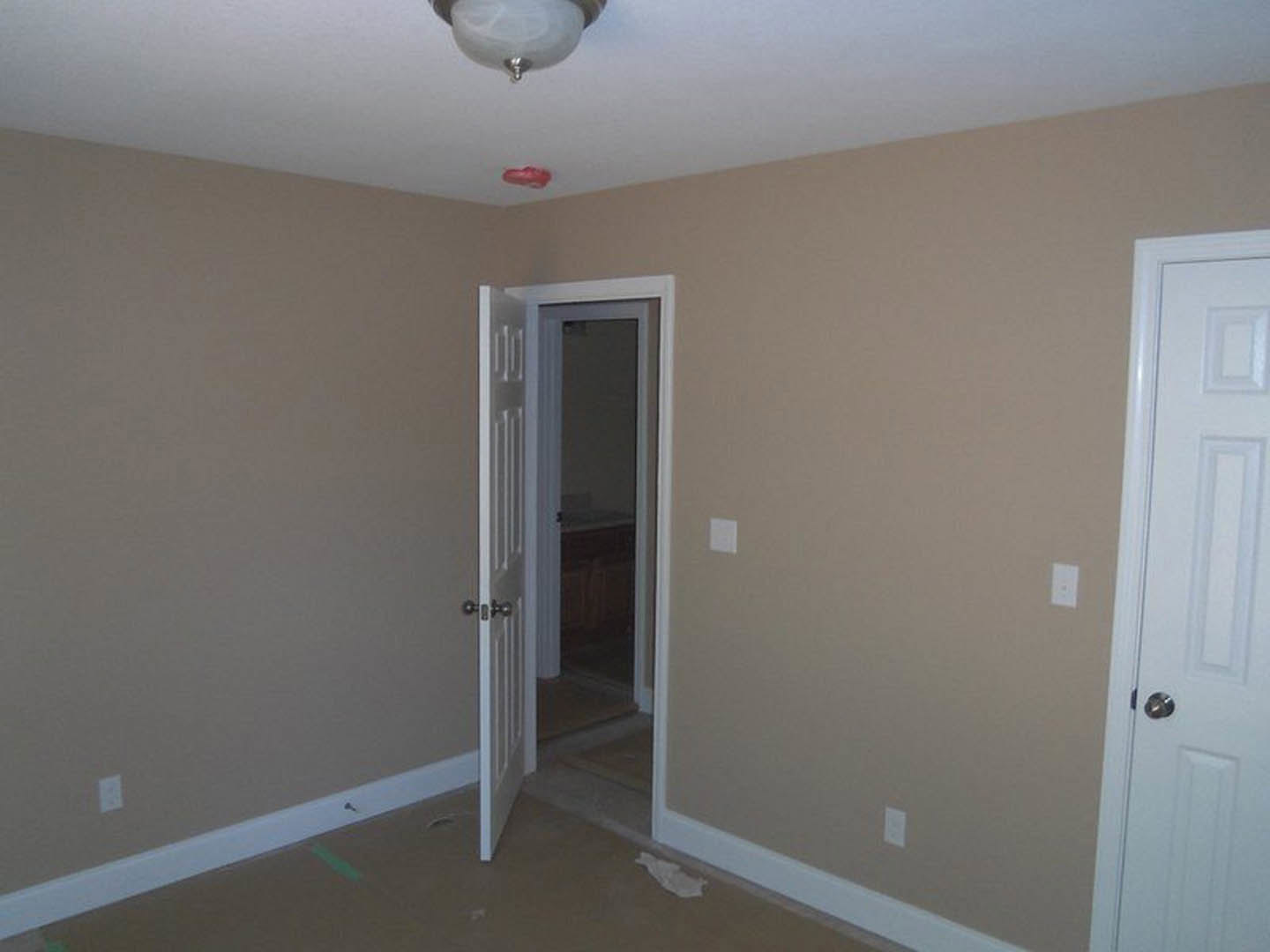 White paneled door with brushed metal handle set in a light grey plaster wall, crown molding detail, and hardwood flooring visible