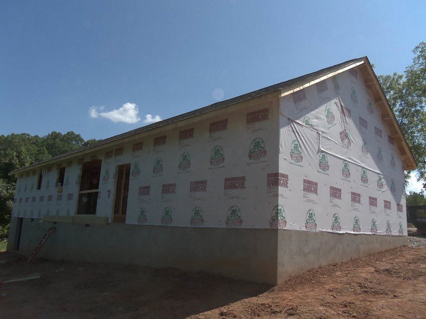 Framed house under construction with plastic sheeting covering exterior walls, exposed insulation, square window, and visible construction markings on plywood.