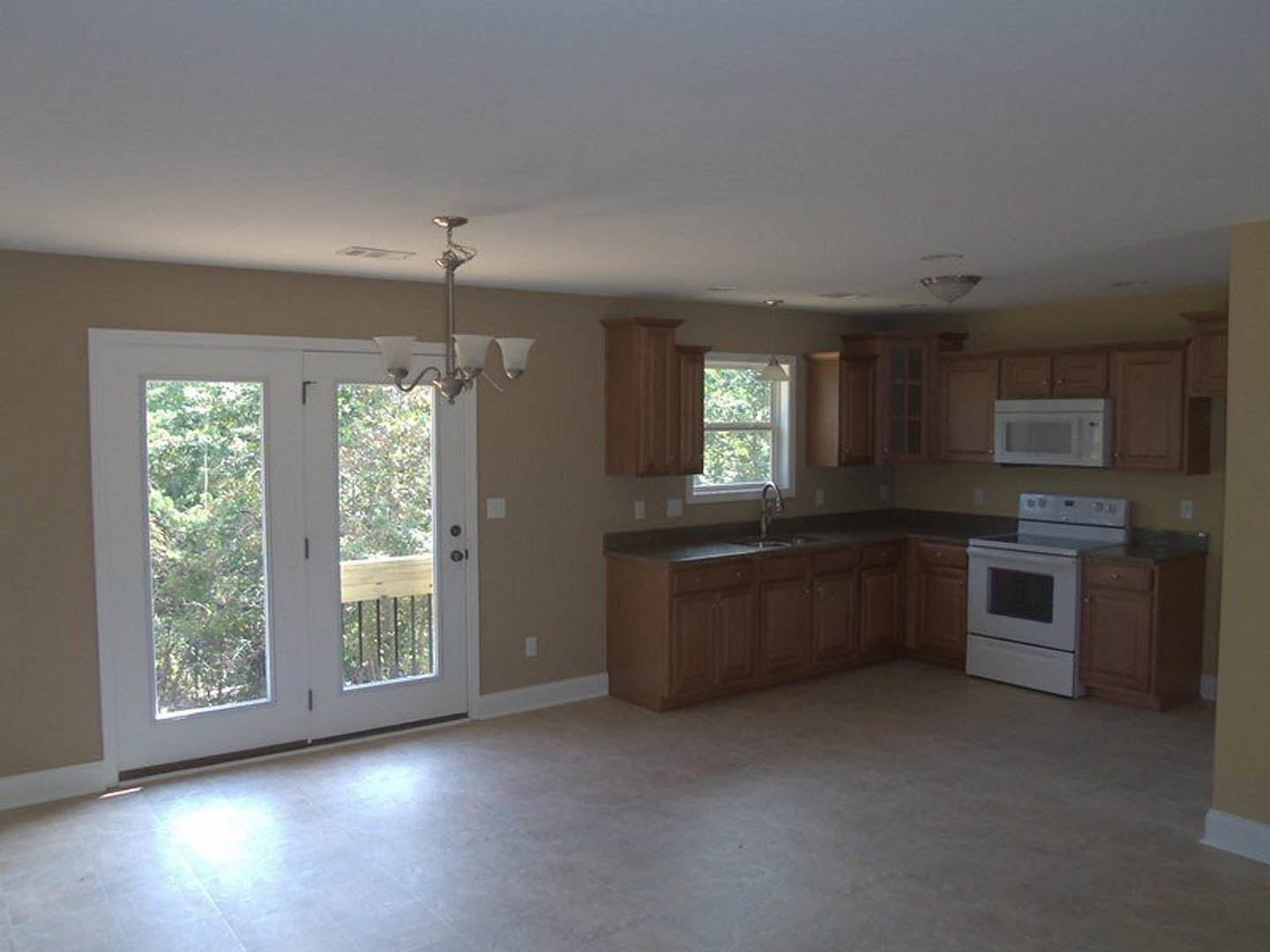 White kitchen with shaker cabinets, white stove and oven, glass-paneled double doors, white microwave, light-colored floor, and a close-up of a crystal chandelier.