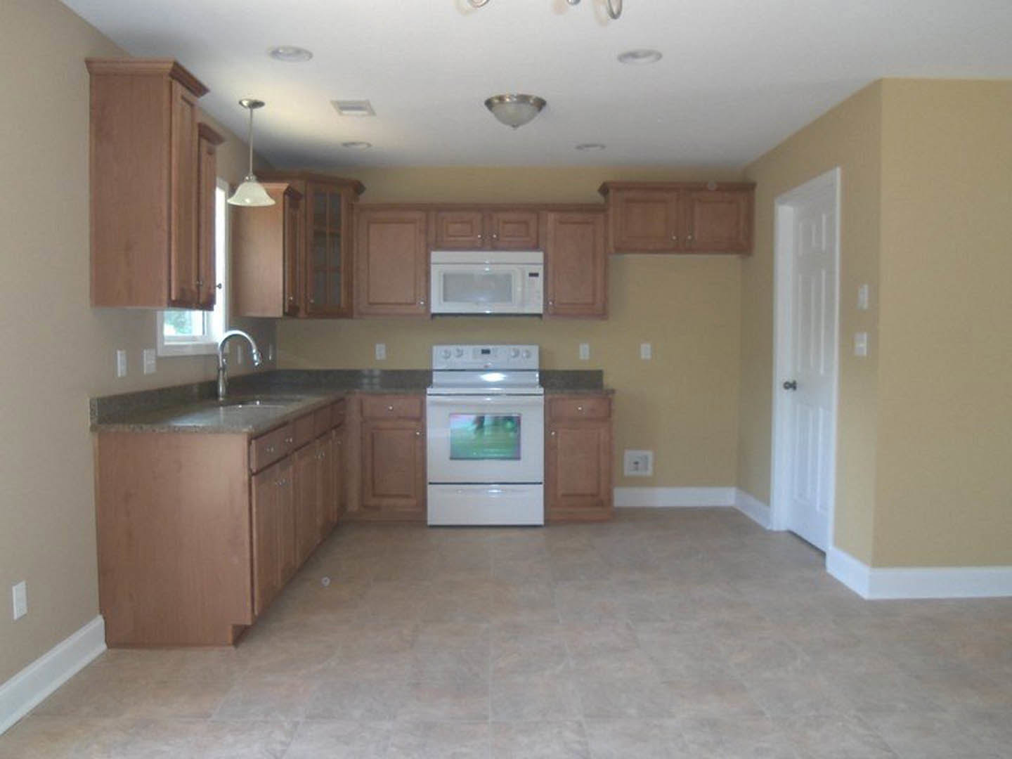 Kitchen with light wood cabinets, white stove and microwave, neutral countertops, stainless faucet, and tile flooring