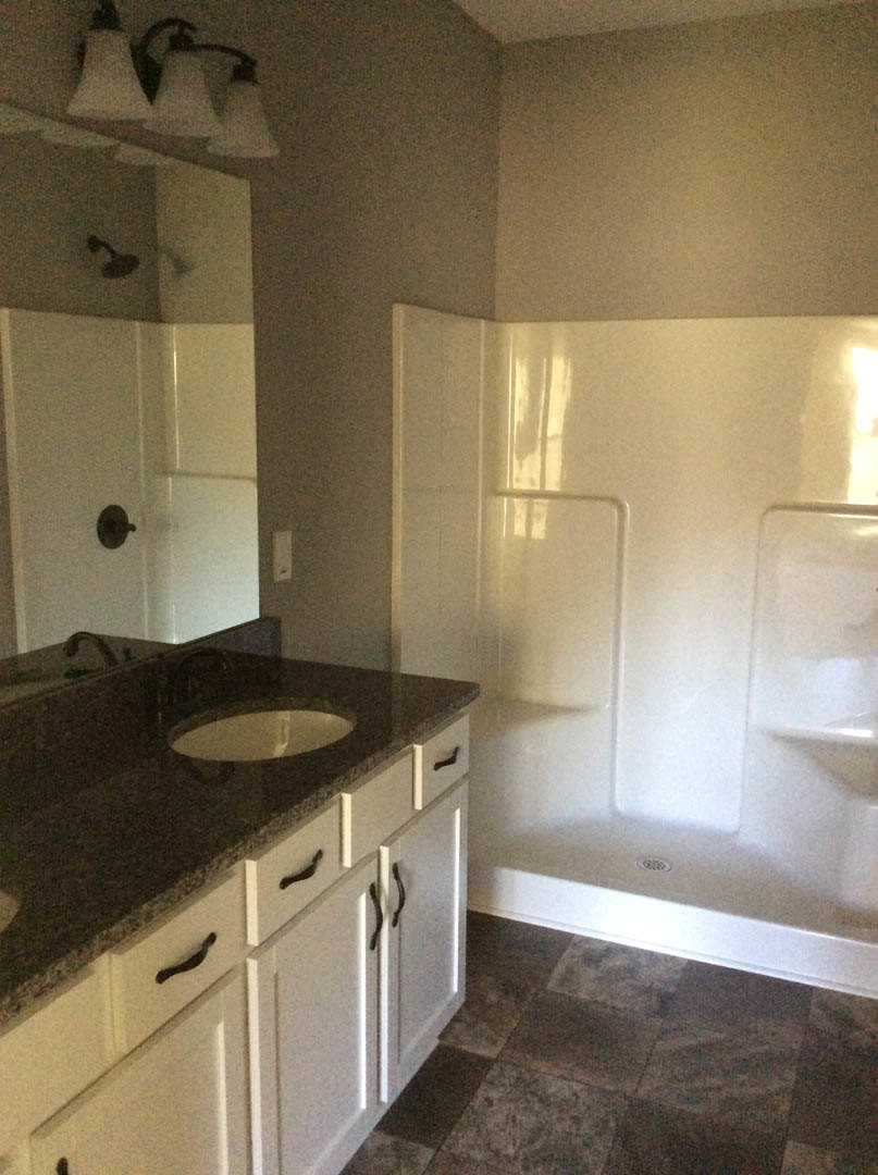 Modern bathroom featuring a granite countertop with undermount sink, chrome faucet, glass-enclosed shower, and light-colored tile flooring