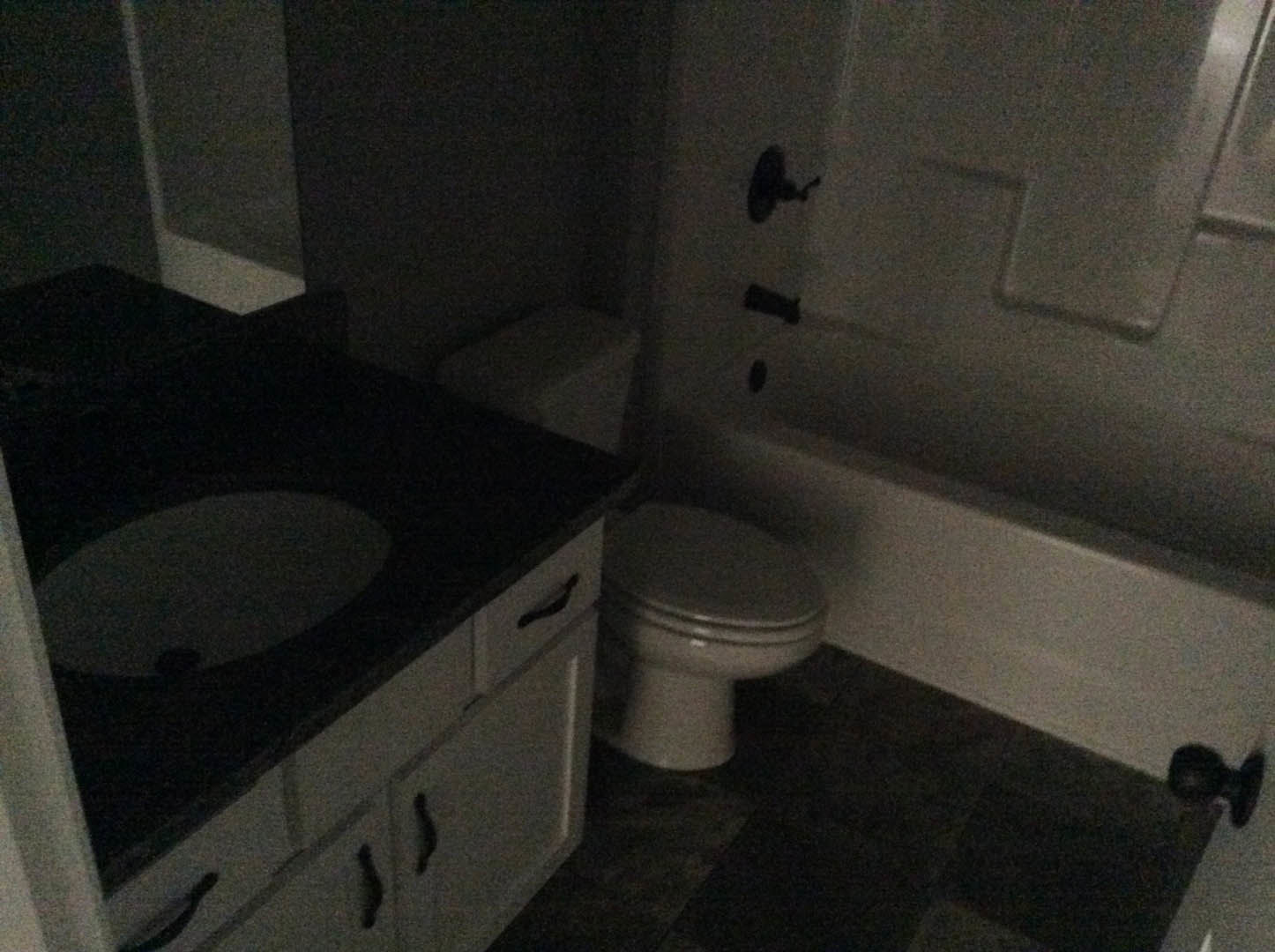 White porcelain sink and toilet with chrome fixtures, light gray tile flooring, white cabinetry, and stone countertop in a modern bathroom.