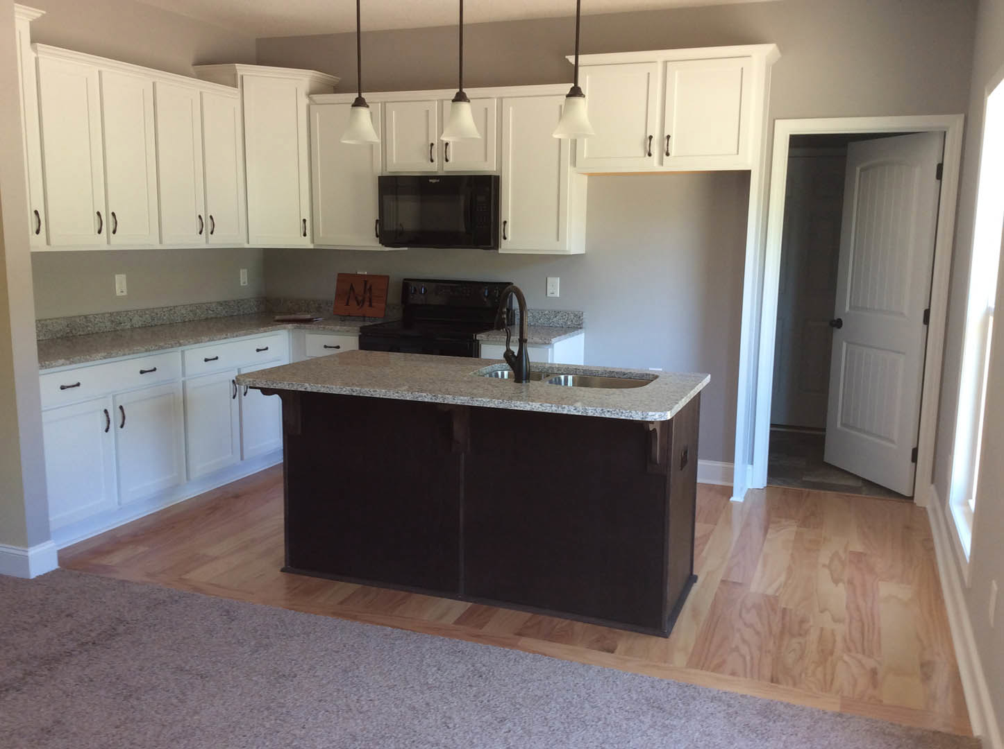 Kitchen with black and white granite countertop, stainless steel sink, white cabinetry with black knobs, black microwave, white door, and carpeted floor adjacent to wall