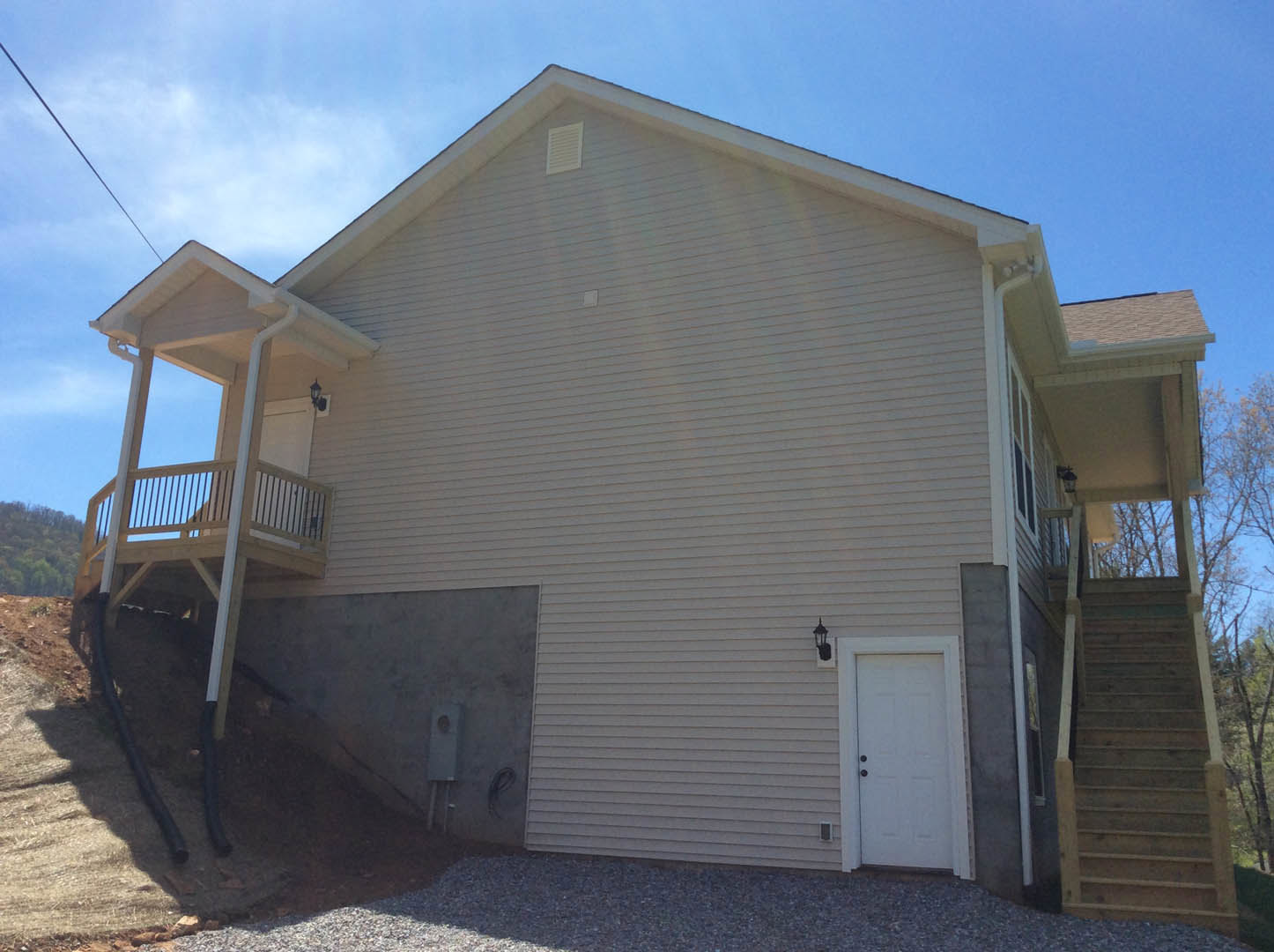 Two-story house with white siding, black-trimmed windows, wooden porch, balcony, and prominent wooden staircase with handrail leading to front entrance.