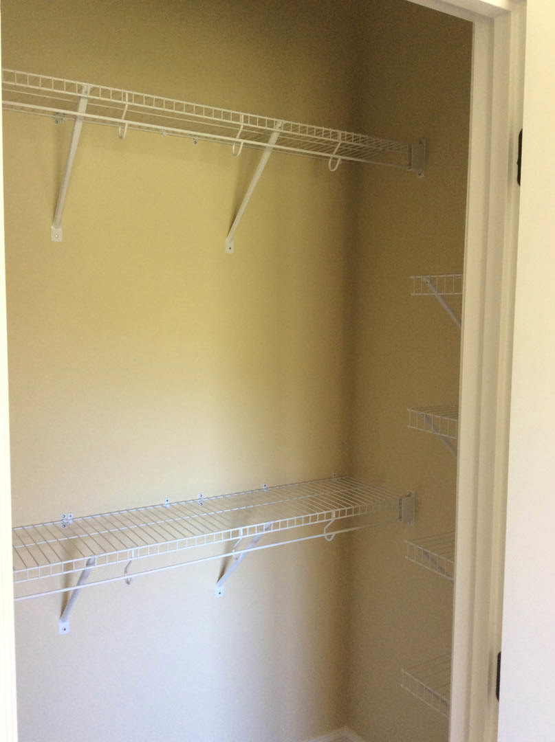 Walk-in closet with white wire shelving on walls and ceiling, white door, plaster walls, and a small ladder leaning against the wall.