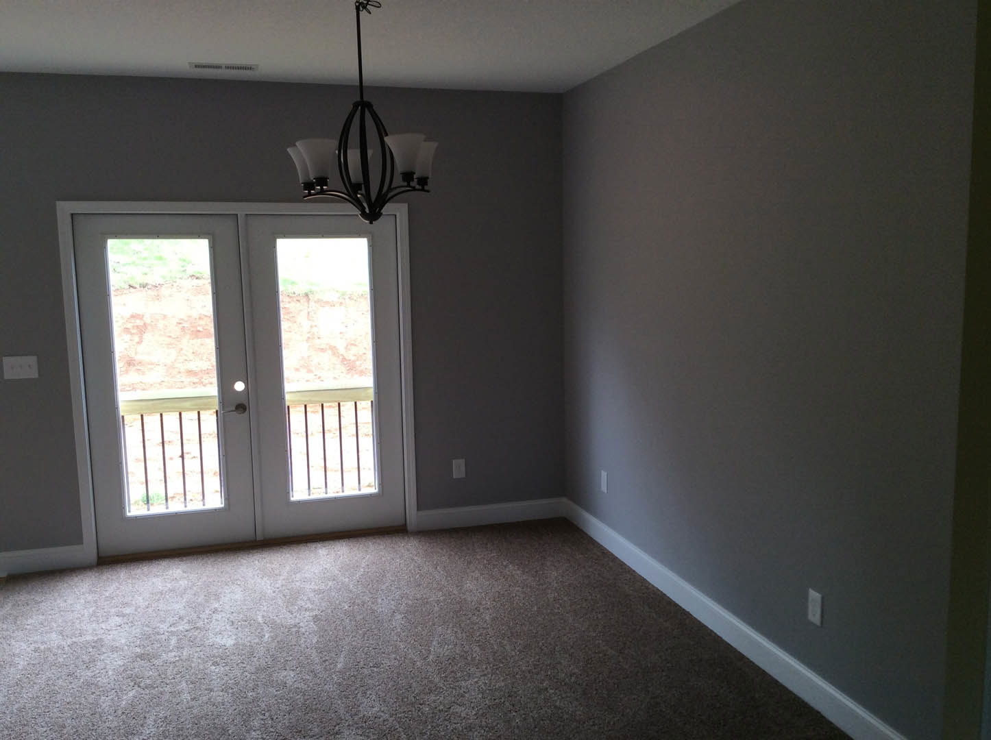 Carpeted room with double glass-paneled doors, ornate chandelier hanging from ceiling, white plaster walls, and dark metal light fixture.
