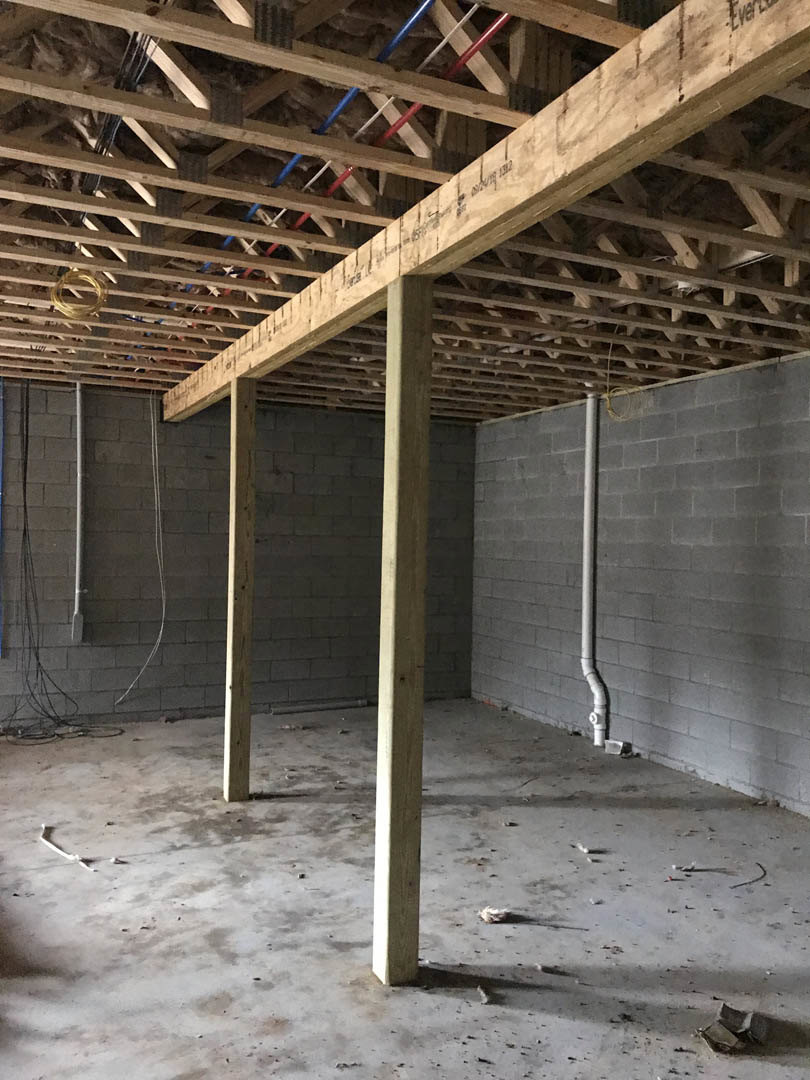 Exposed wooden ceiling beam crossing a modern room with white walls, visible steel wire and pipe along the wall, composite flooring, and plank accents.