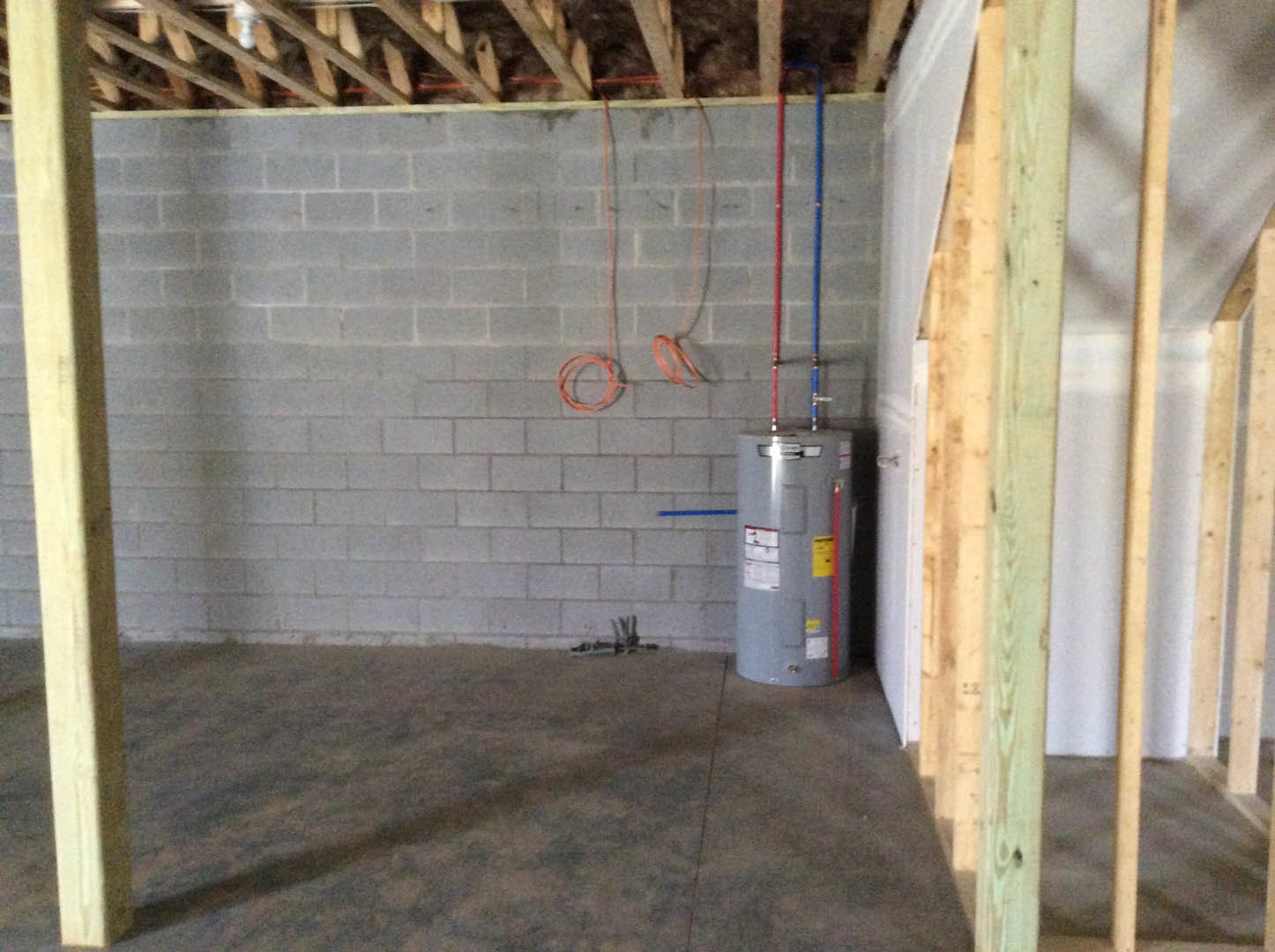 Grey cylindrical tank positioned in a room featuring an exposed brick wall, wood beam ceiling, and unfinished floor.