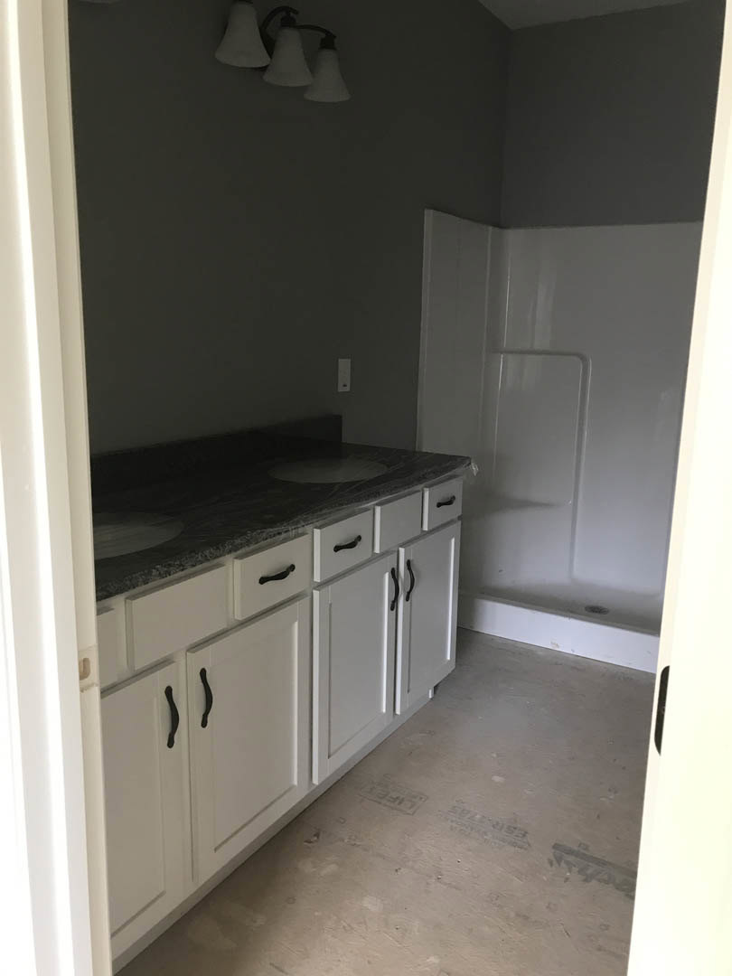 Bathroom with white cabinets, black handles, white countertop, undermount sink, glass-enclosed shower, white tile walls, and recessed lighting.