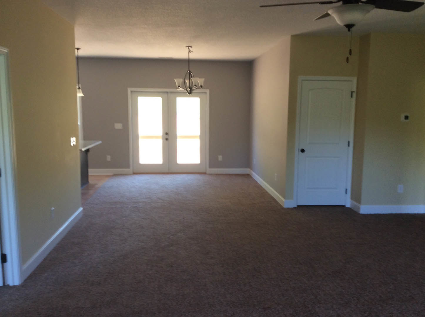 Carpeted room with white double doors, black handles, ceiling fan, and rectangular window letting in natural light