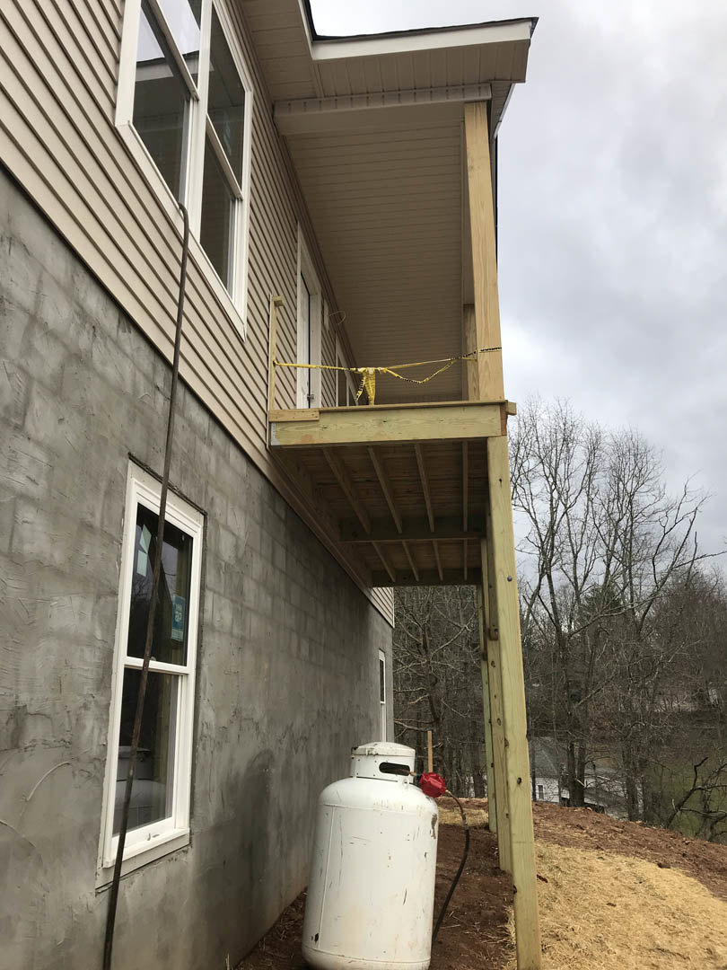 White cylindrical tank with red handle mounted on exterior wall near window; leafless trees and cloudy sky in background.